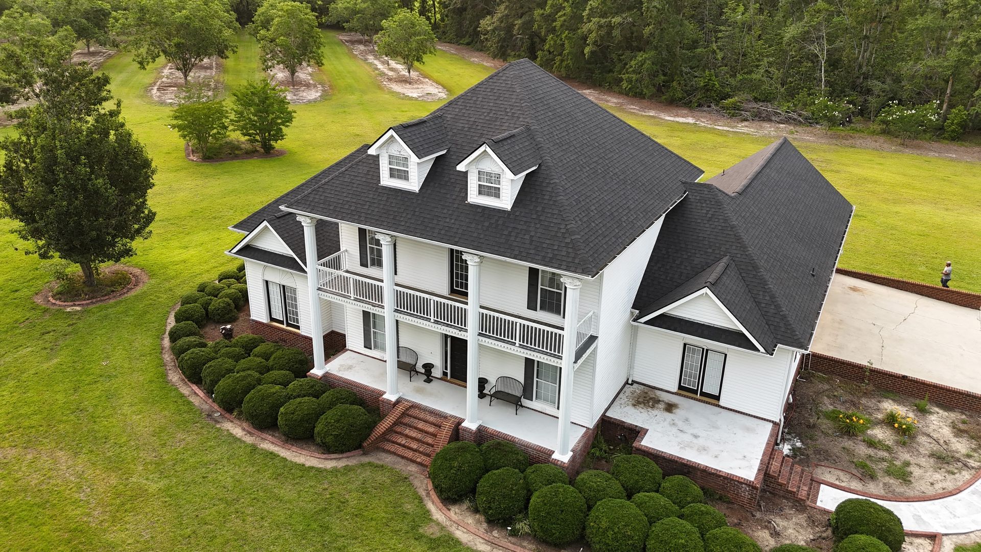 White two-story house with a dark roof, porch, and landscaping in a green yard.