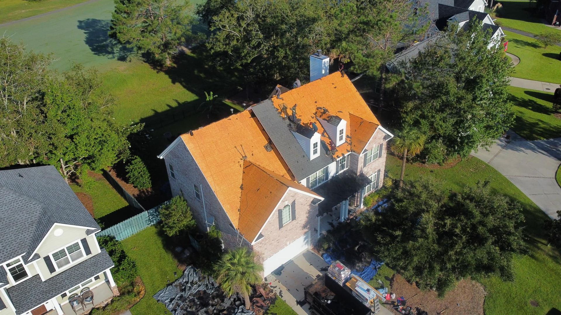 House with a partially replaced orange roof, surrounded by green lawns and trees.