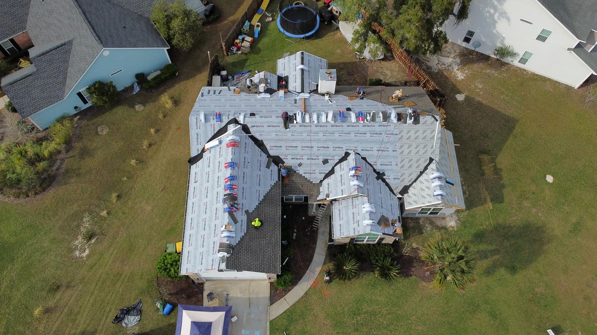 Aerial view of a house with roof partially under construction; workers on roof, surrounded by yard and other houses.