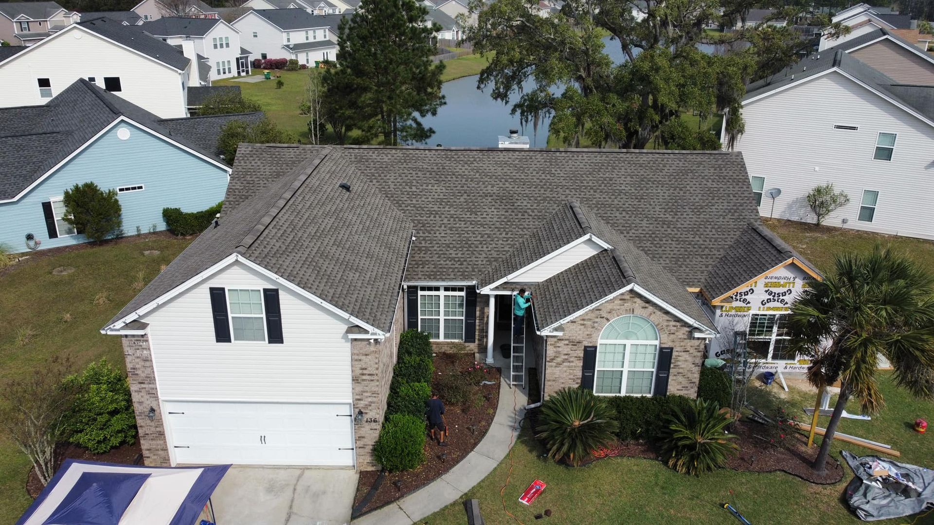 Overhead view of a suburban home with a grey roof, brick and white siding, and a palm tree in front.