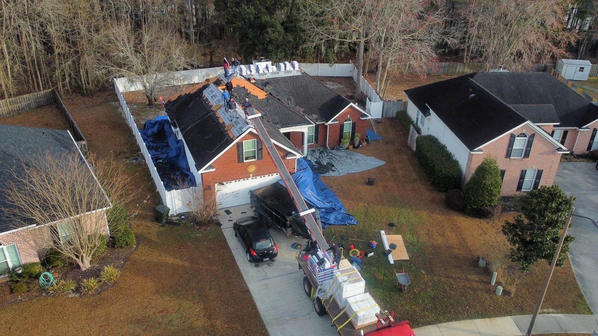 Roofers replacing shingles on a house, with a crane delivering supplies.