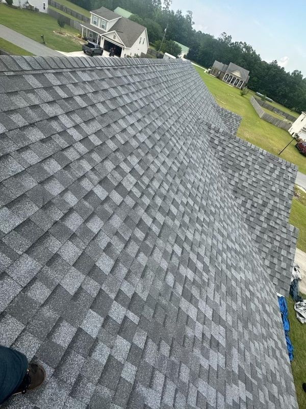 Gray shingled roof on a house with other houses in the background on a sunny day.