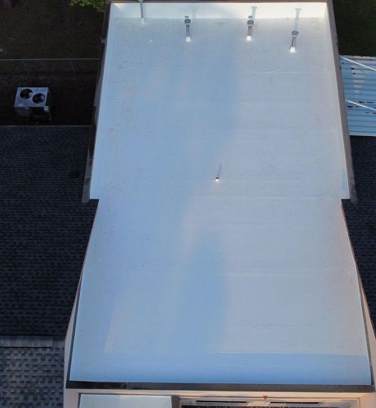 Overhead view of a white roof with lights, next to a dark roof and an air conditioning unit.