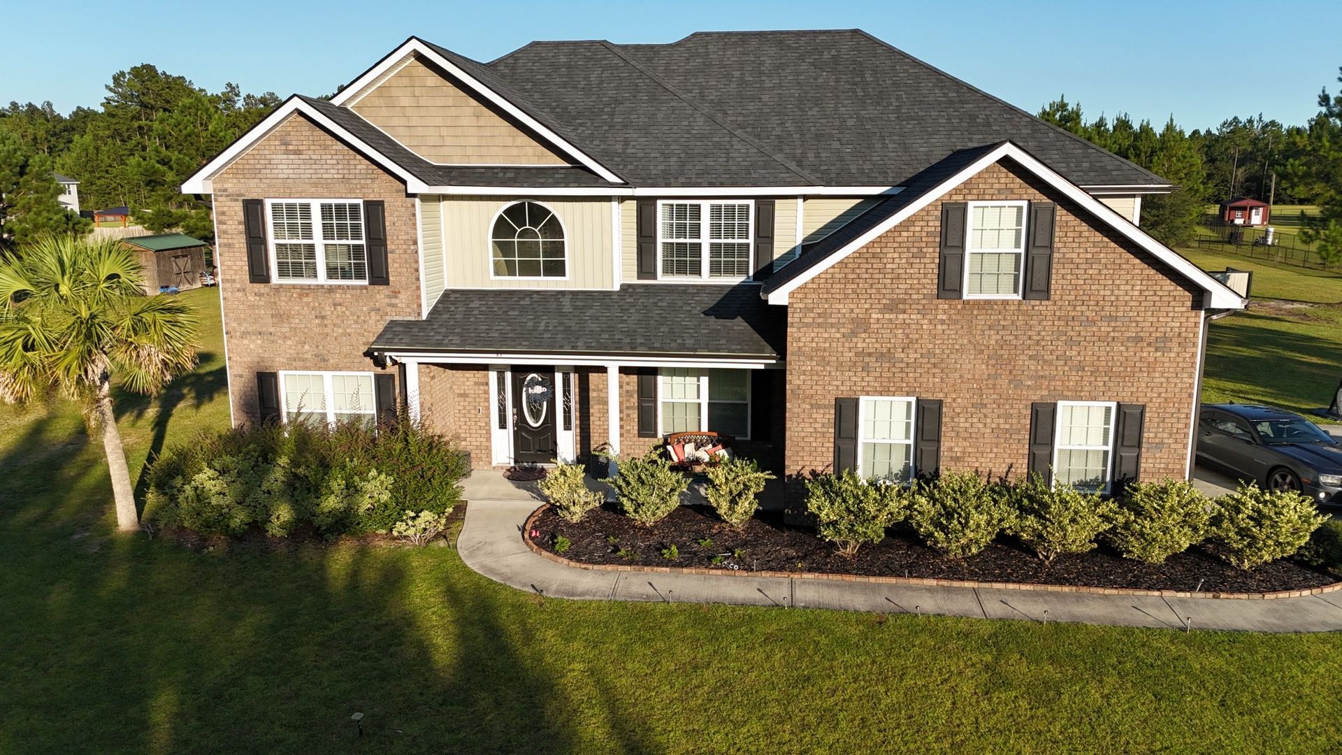 Two-story brick house with black shutters, a dark roof, and green lawn.