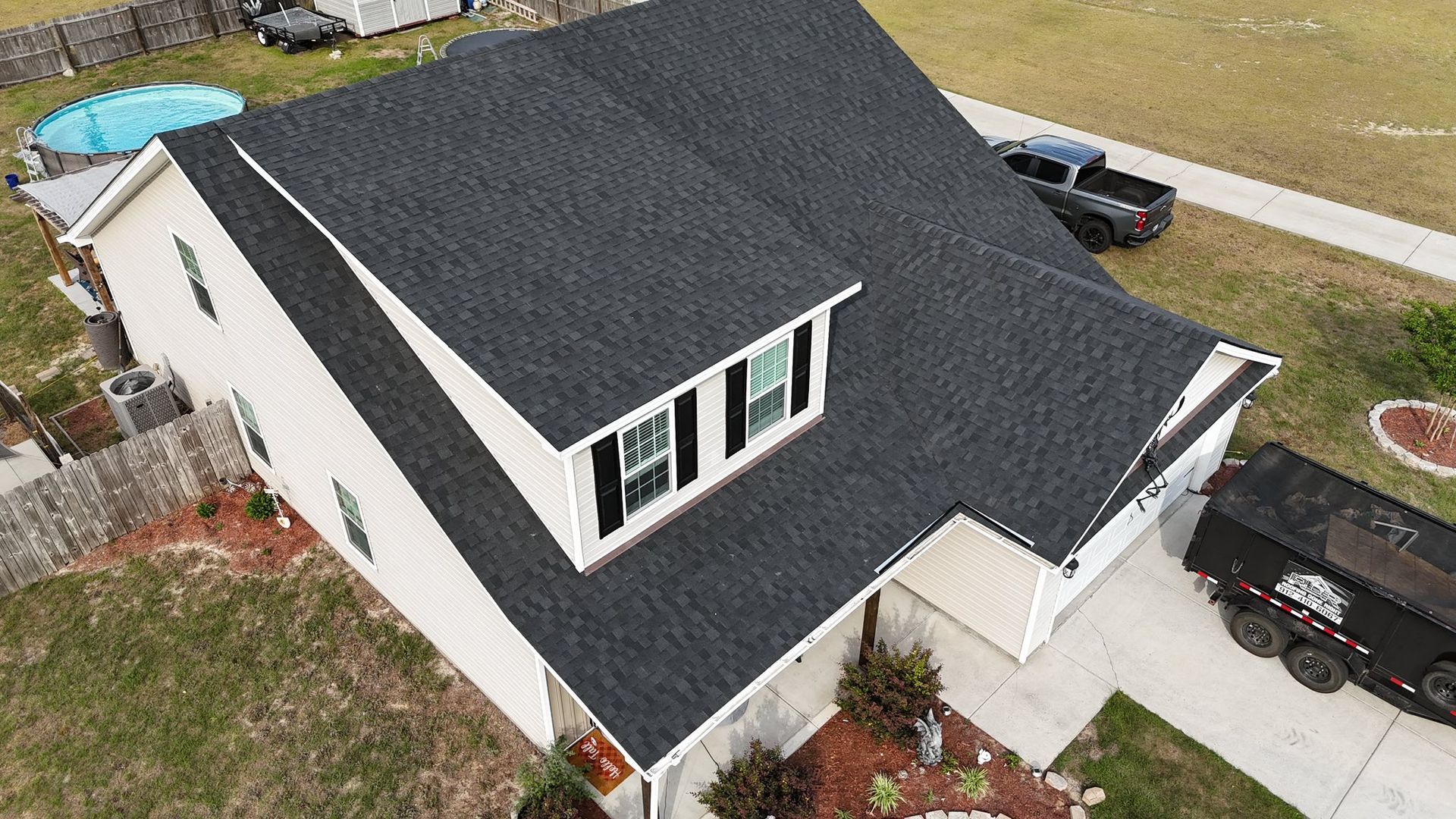 Aerial view of a house with a dark gray roof, beige siding, and a black truck parked outside.