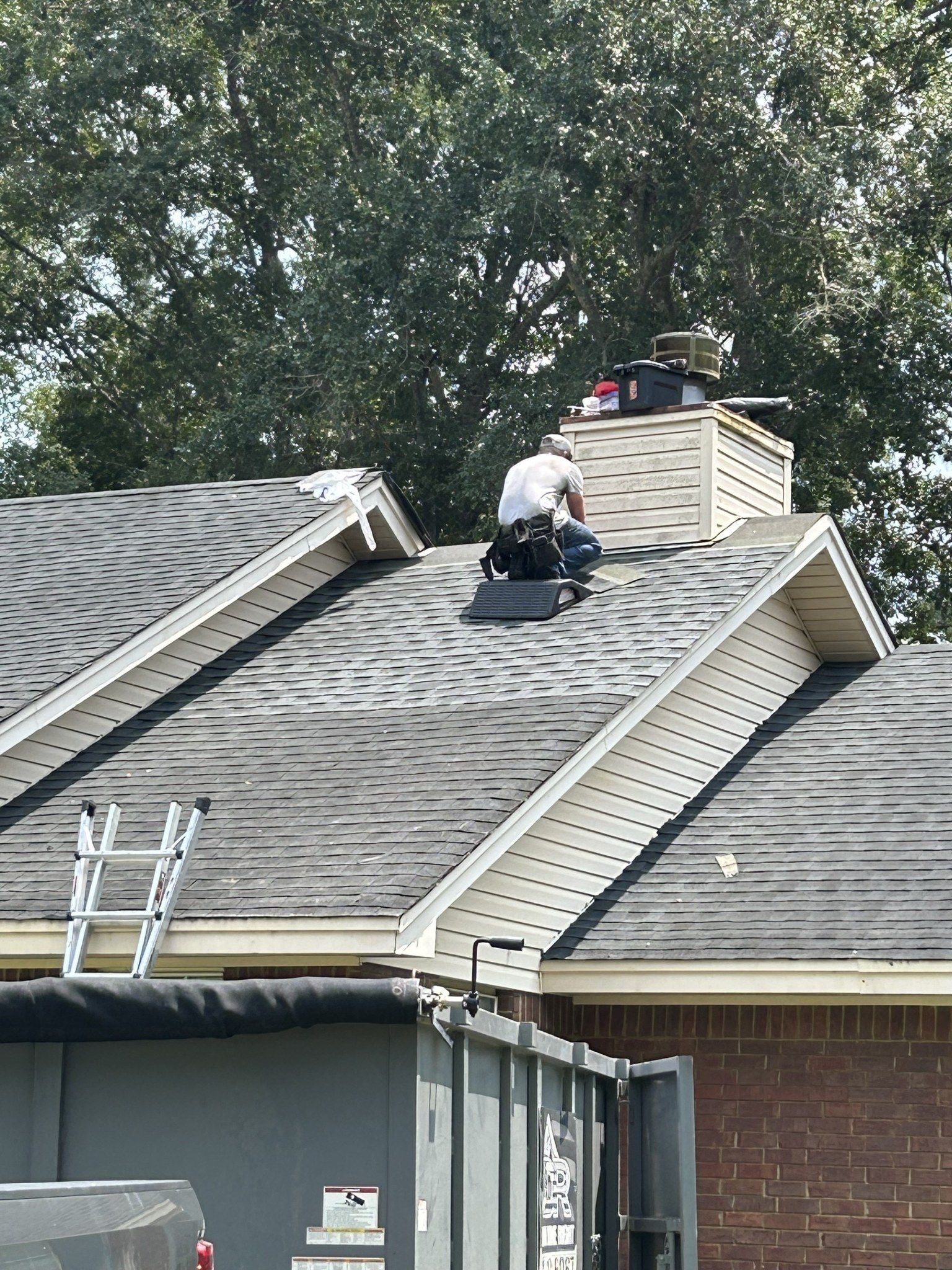 Roofer on a roof, repairing a chimney. Ladder on the roof, dumpster below.