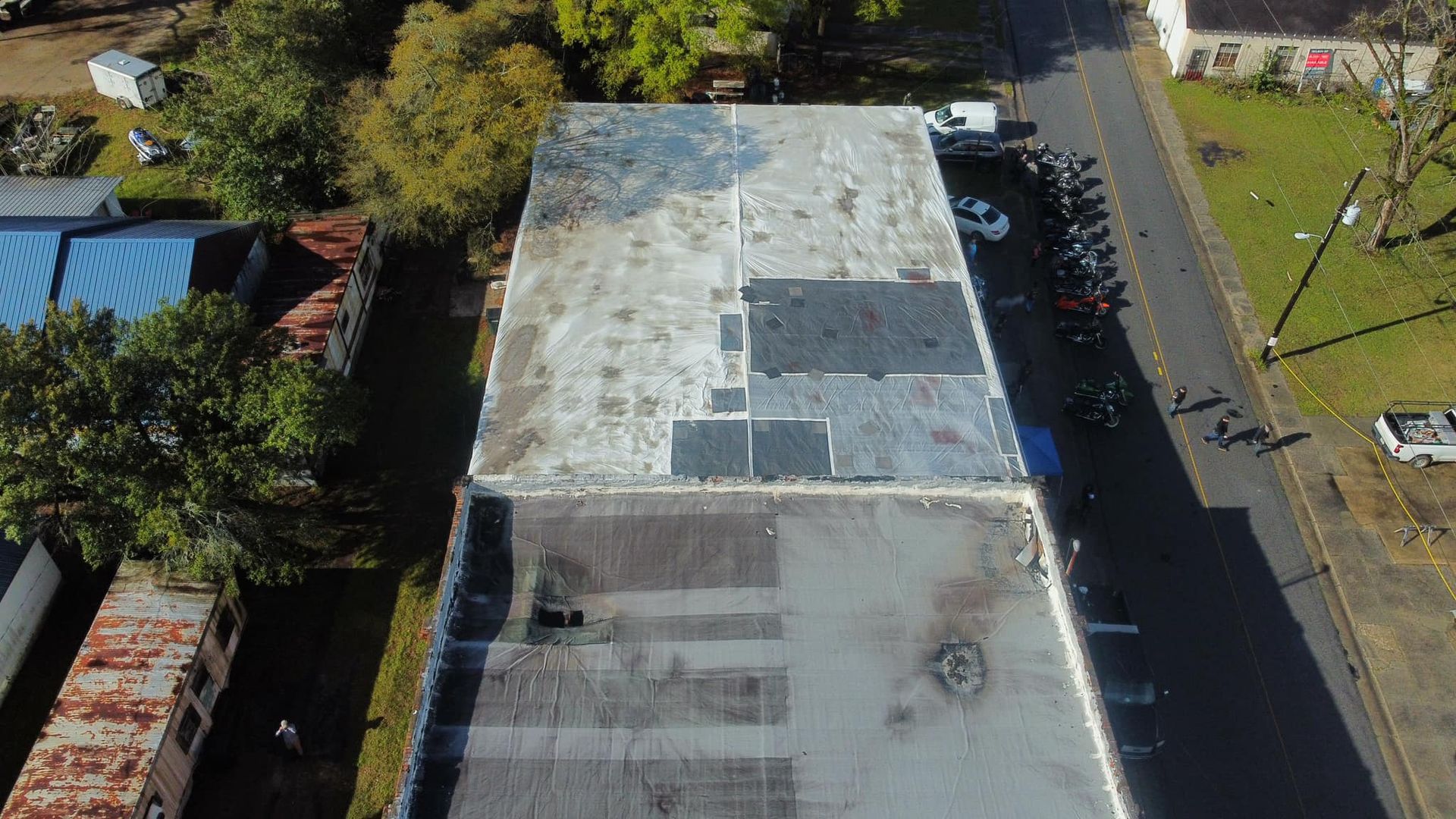 Overhead view of a two-story building with a weathered roof next to a street lined with parked cars.