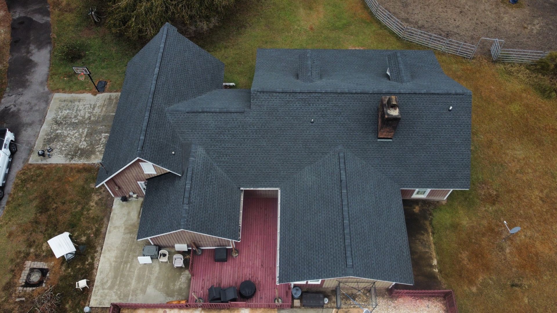 Overhead view of a house with dark gray roof, brown deck, and chimney on a lawn.