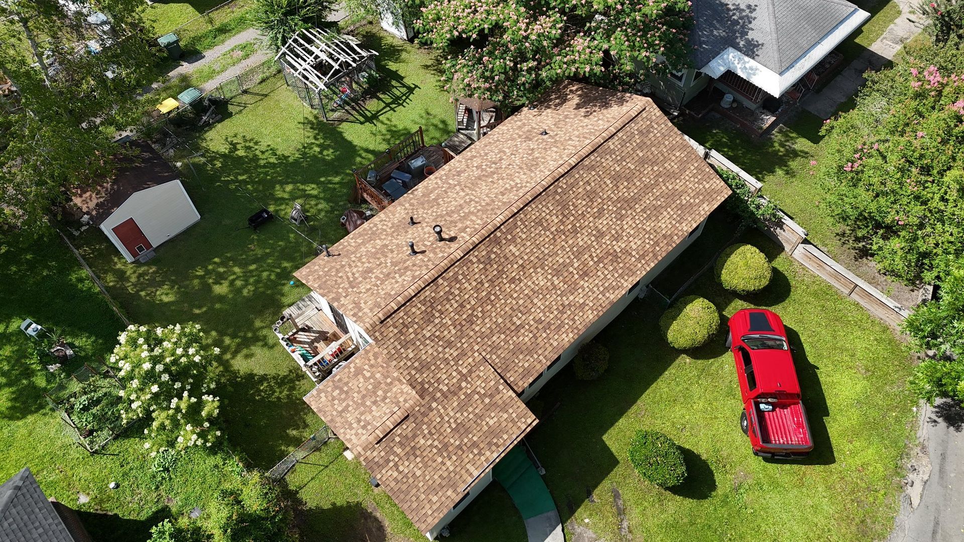 Aerial view of a house with a brown roof, red truck parked in front, and lush green yard.