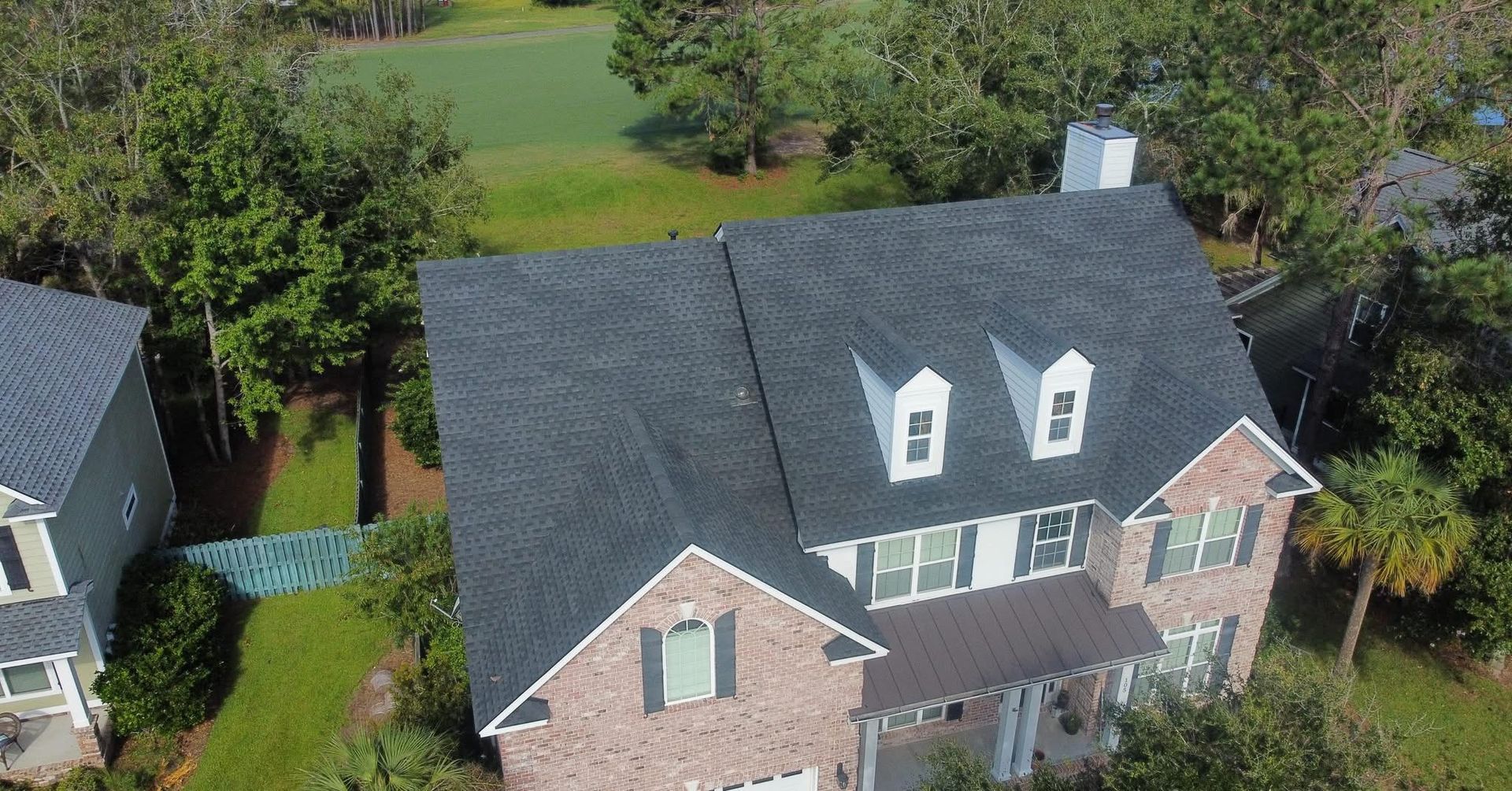 Aerial view of a two-story house with a dark roof, brick exterior, and three dormer windows.
