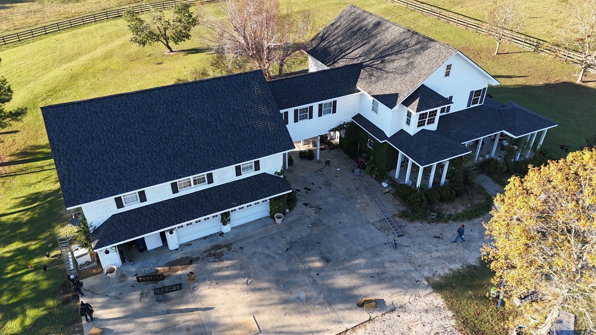 Large white house with black roof, driveway, and vineyard in the background.