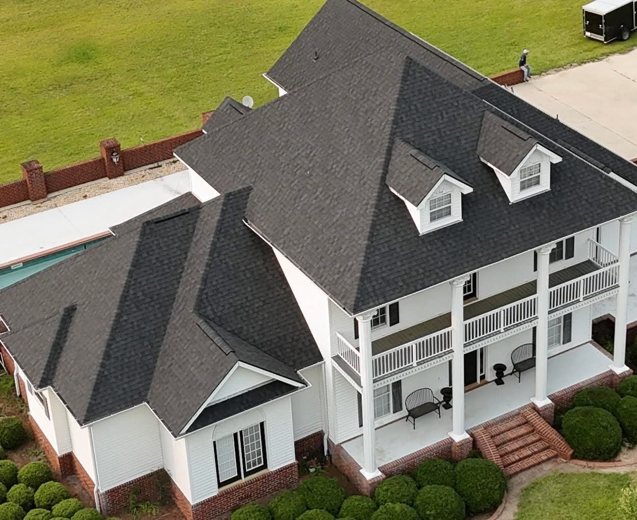 Aerial view of a white house with a dark gray roof, two dormers, and a front porch.