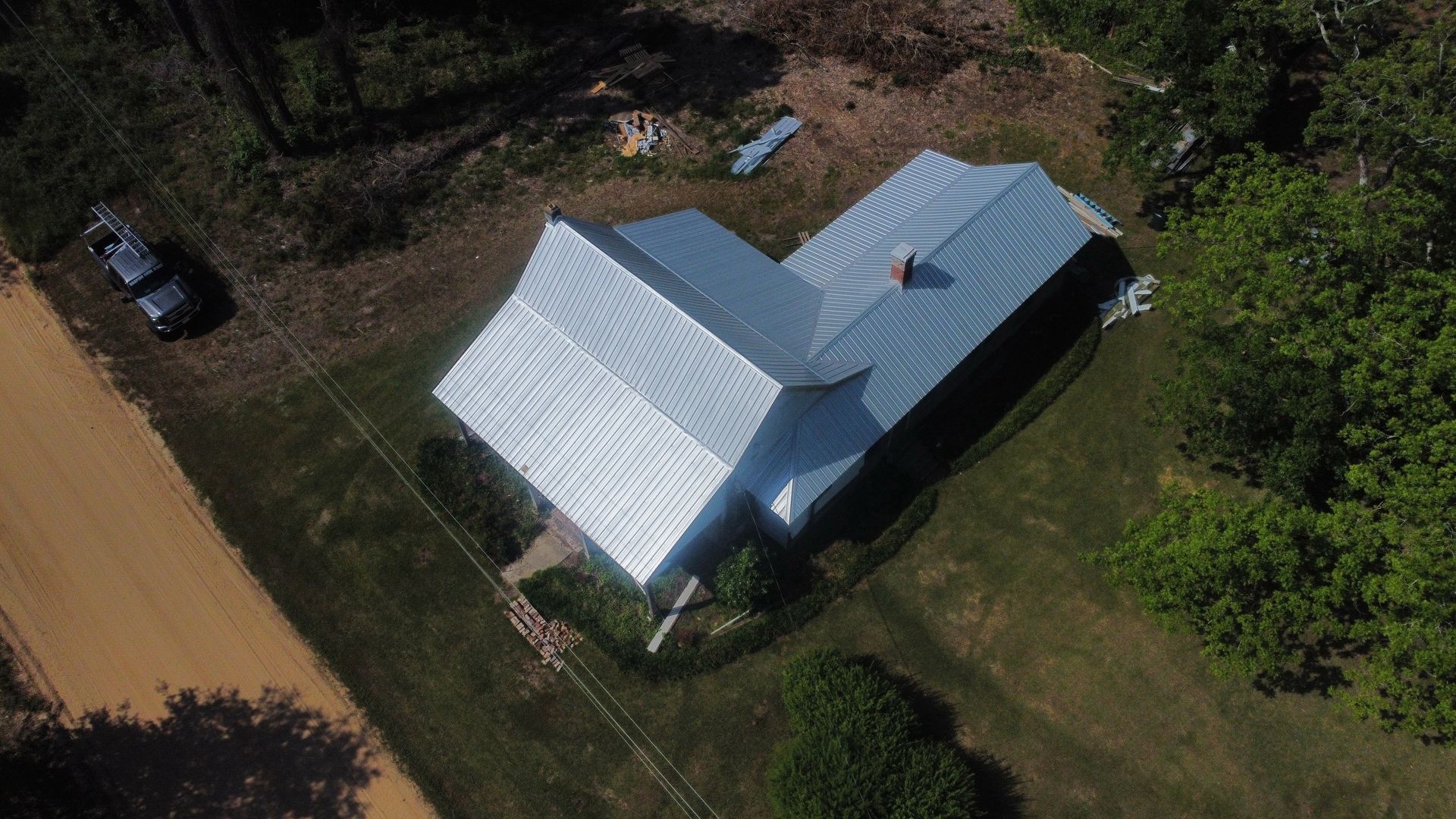 Aerial view of a house with a metal roof surrounded by trees and a dirt road.