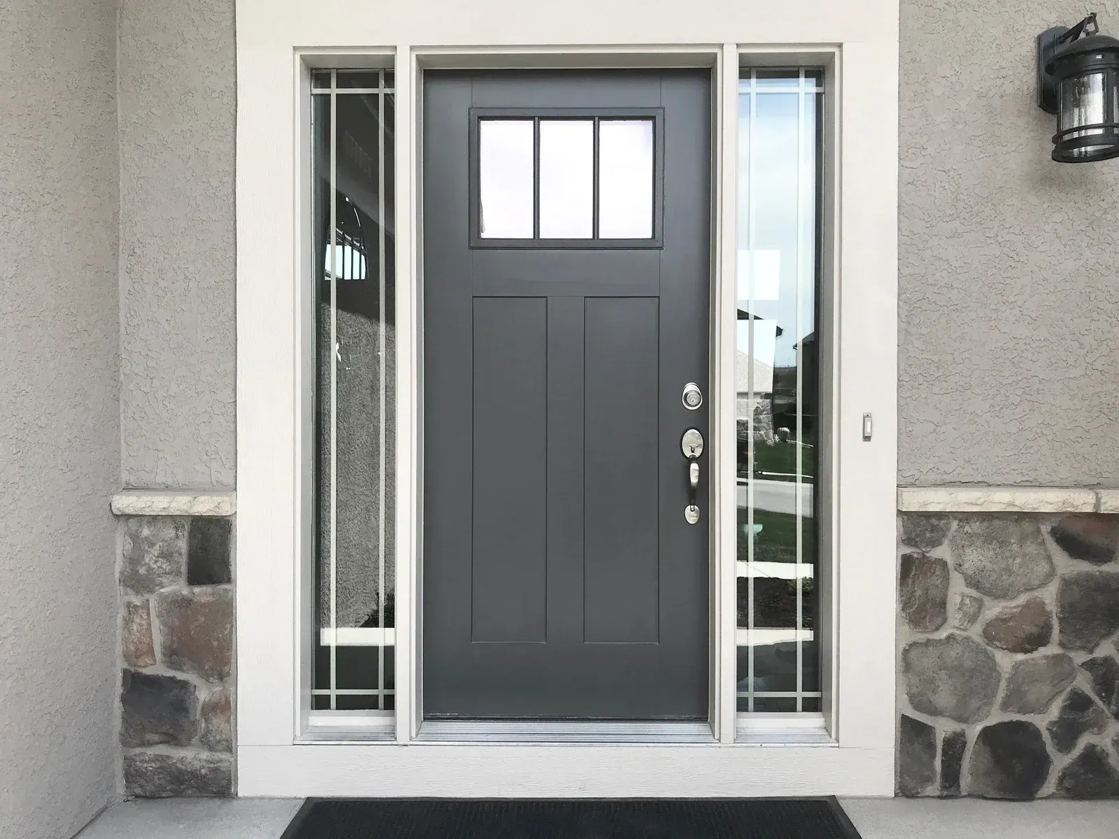 Gray front door with sidelights and stone and stucco exterior.