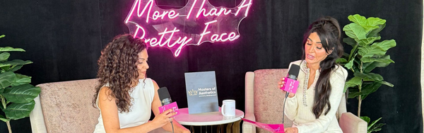Two people sitting in armchairs during a podcast recording, with a neon sign.