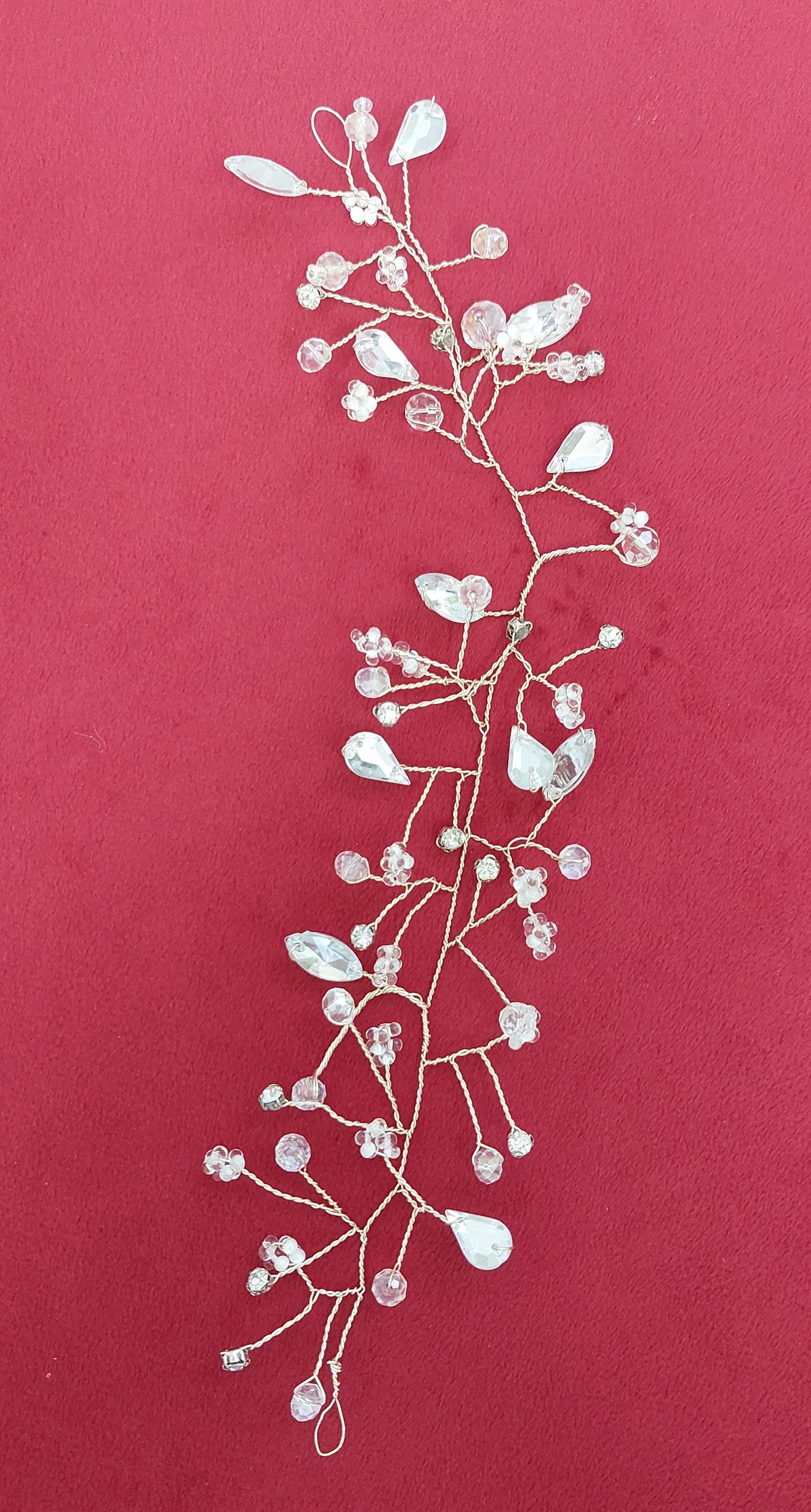 Filo d'argento per capelli con cristalli trasparenti e gemme a forma di lacrima su sfondo marrone.