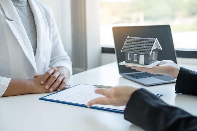A woman is sitting at a table holding a model house.