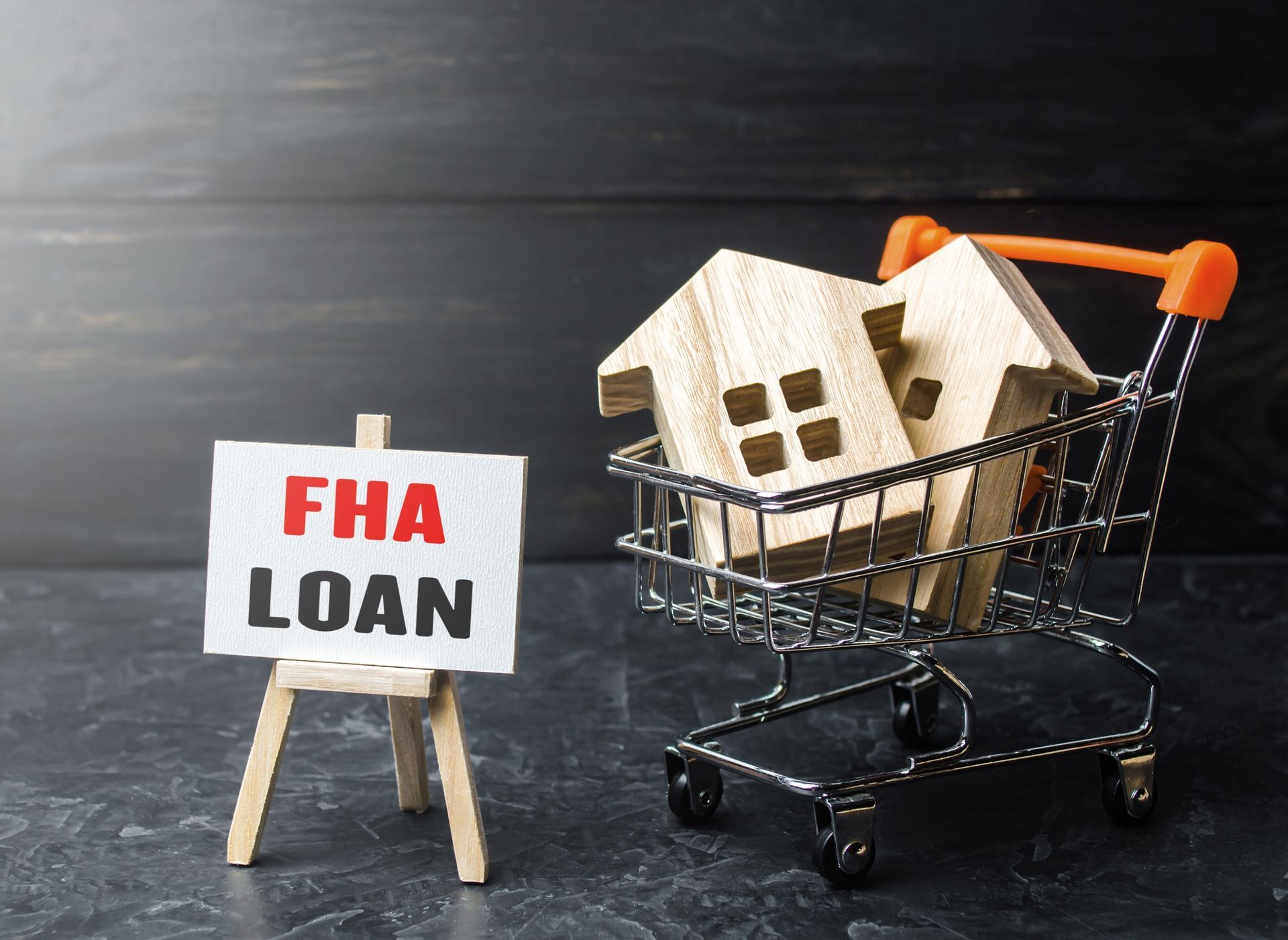 A shopping cart filled with wooden houses next to a sign that says FHA loan.