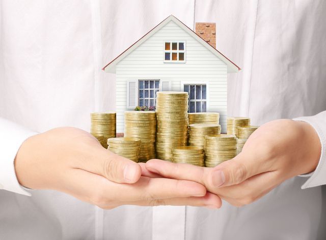 A person is holding a stack of coins in front of a house.