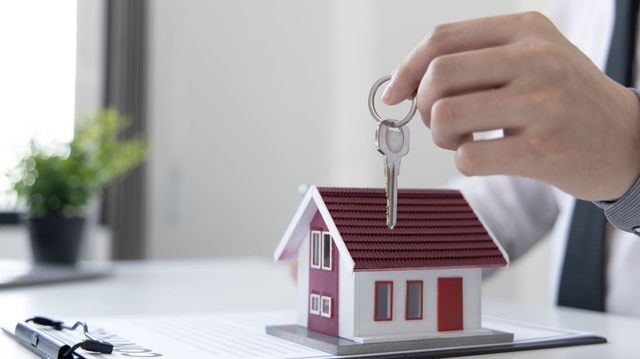 A person is holding a key over a model house.