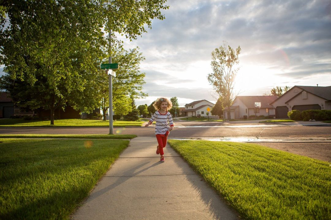 A little girl is running down a sidewalk in a residential neighborhood.