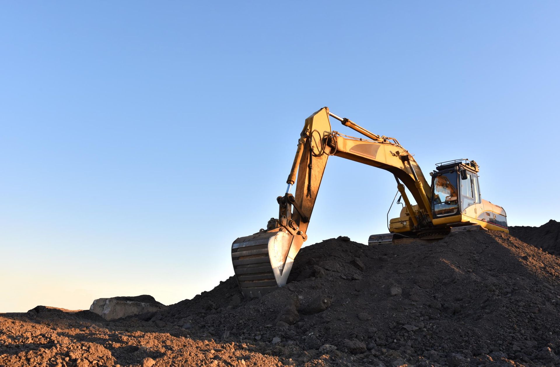 A yellow excavator is sitting on top of a pile of dirt.