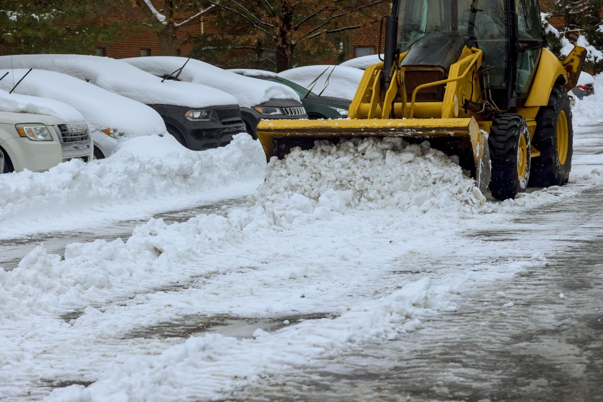 A yellow snow plow is clearing snow from a parking lot.