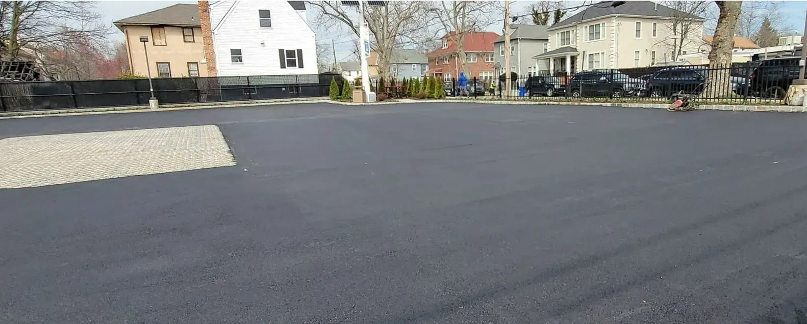 A large asphalt parking lot with houses in the background.