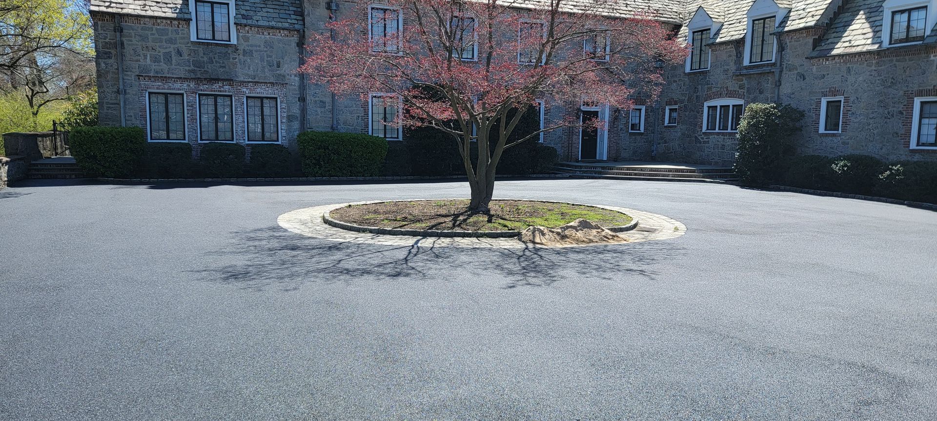 There is a tree in the middle of a driveway in front of a large house.
