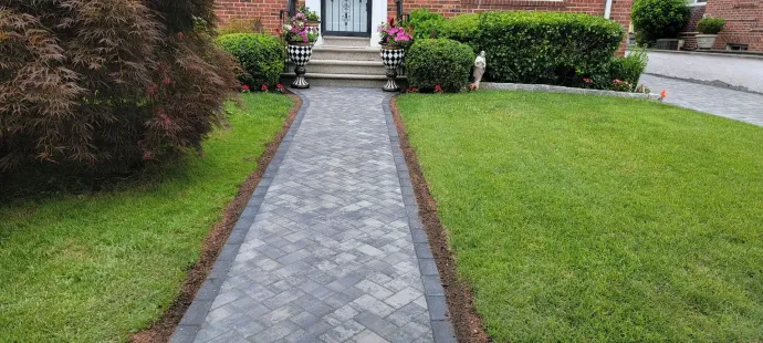 A brick walkway leading to a house with a lush green lawn.