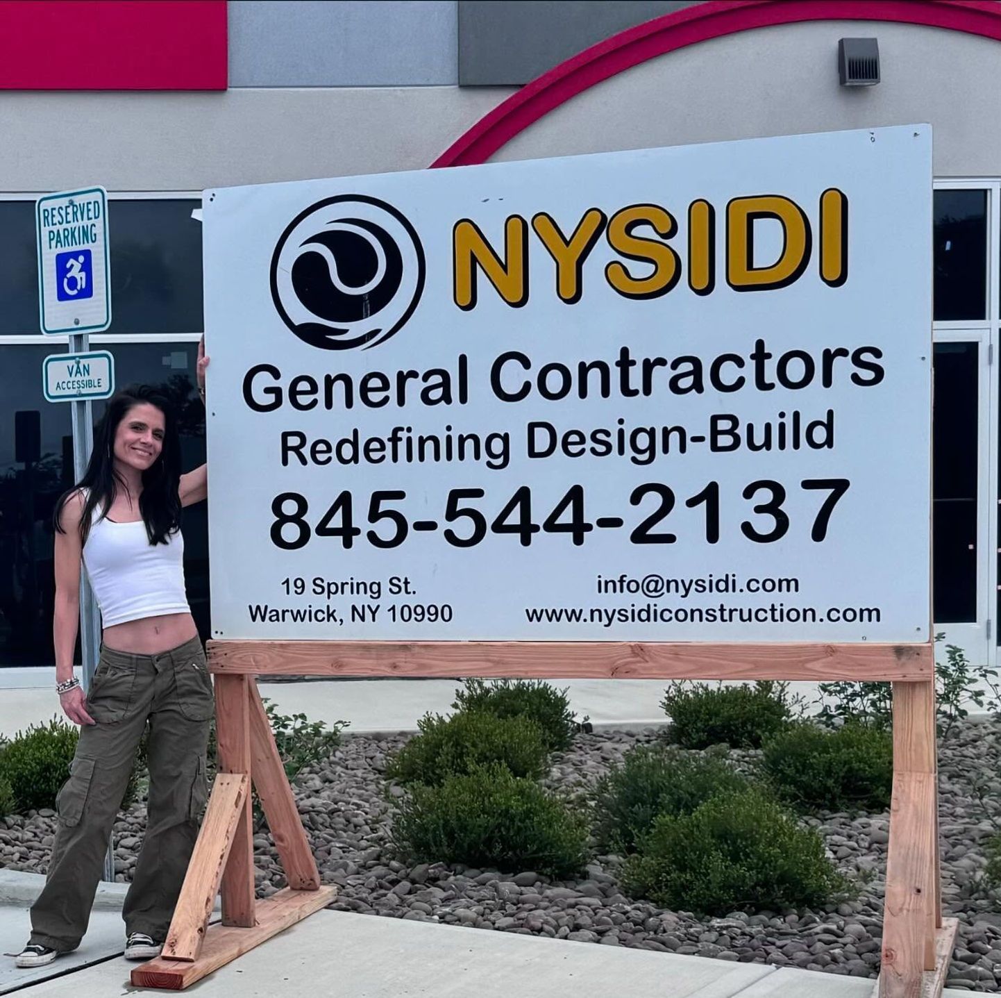 Woman next to NYSIDI General Contractors sign with contact info, located in Warwick, NY.
