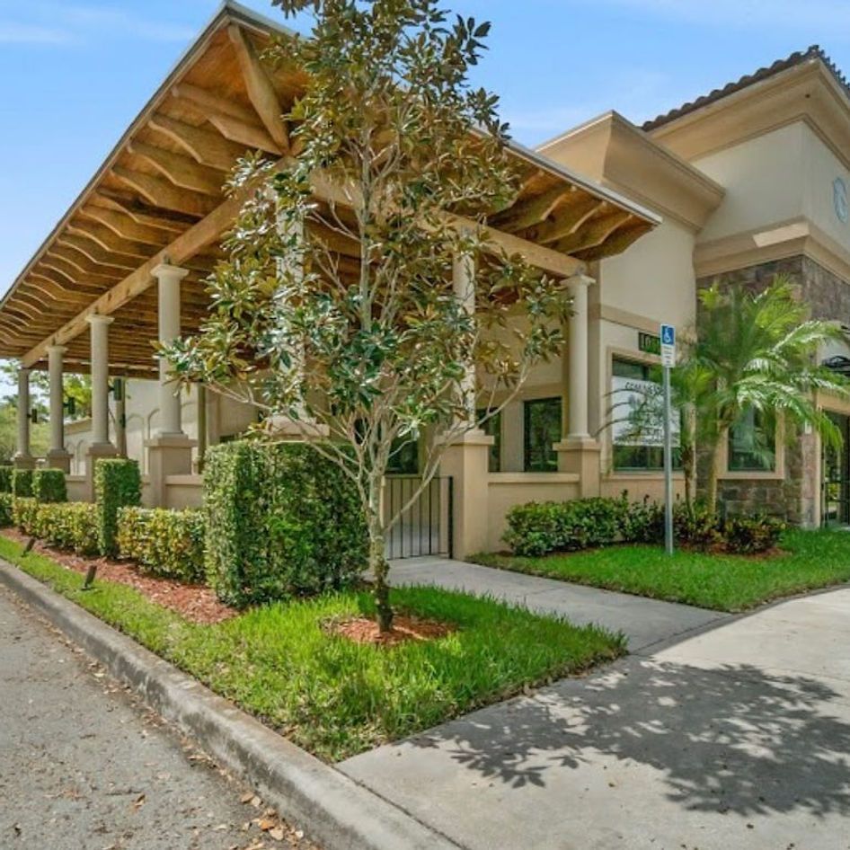 Building with columns, covered walkway, landscaping, and blue handicap parking sign.