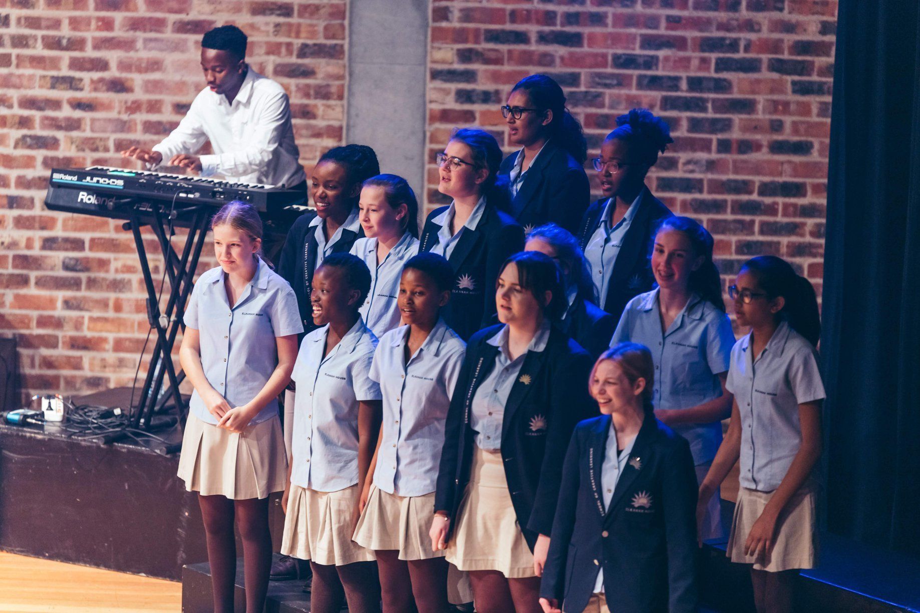 A group of young girls are standing in front of a man playing a keyboard.