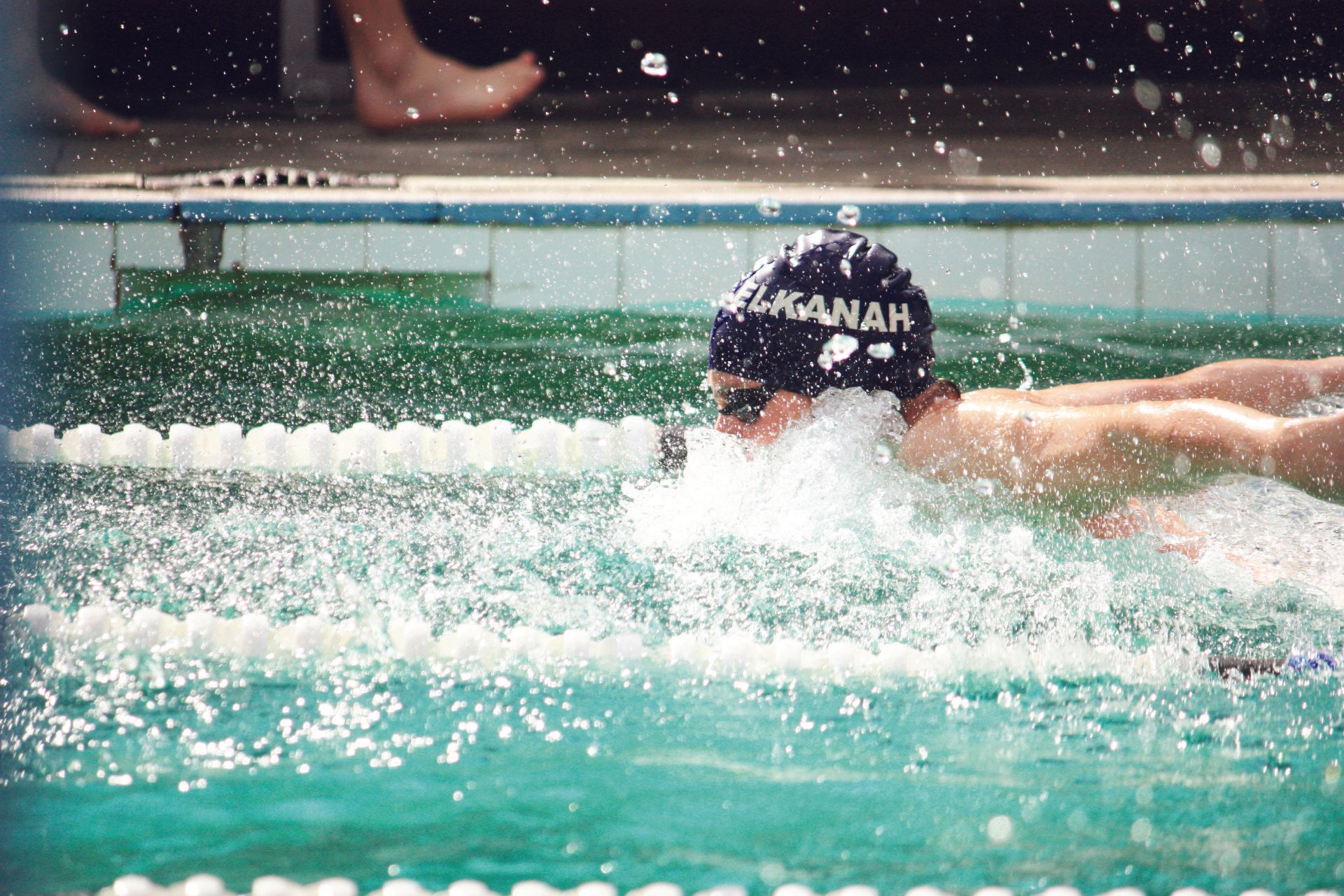 A man is swimming in a pool with a hat that says ' amanah ' on it.