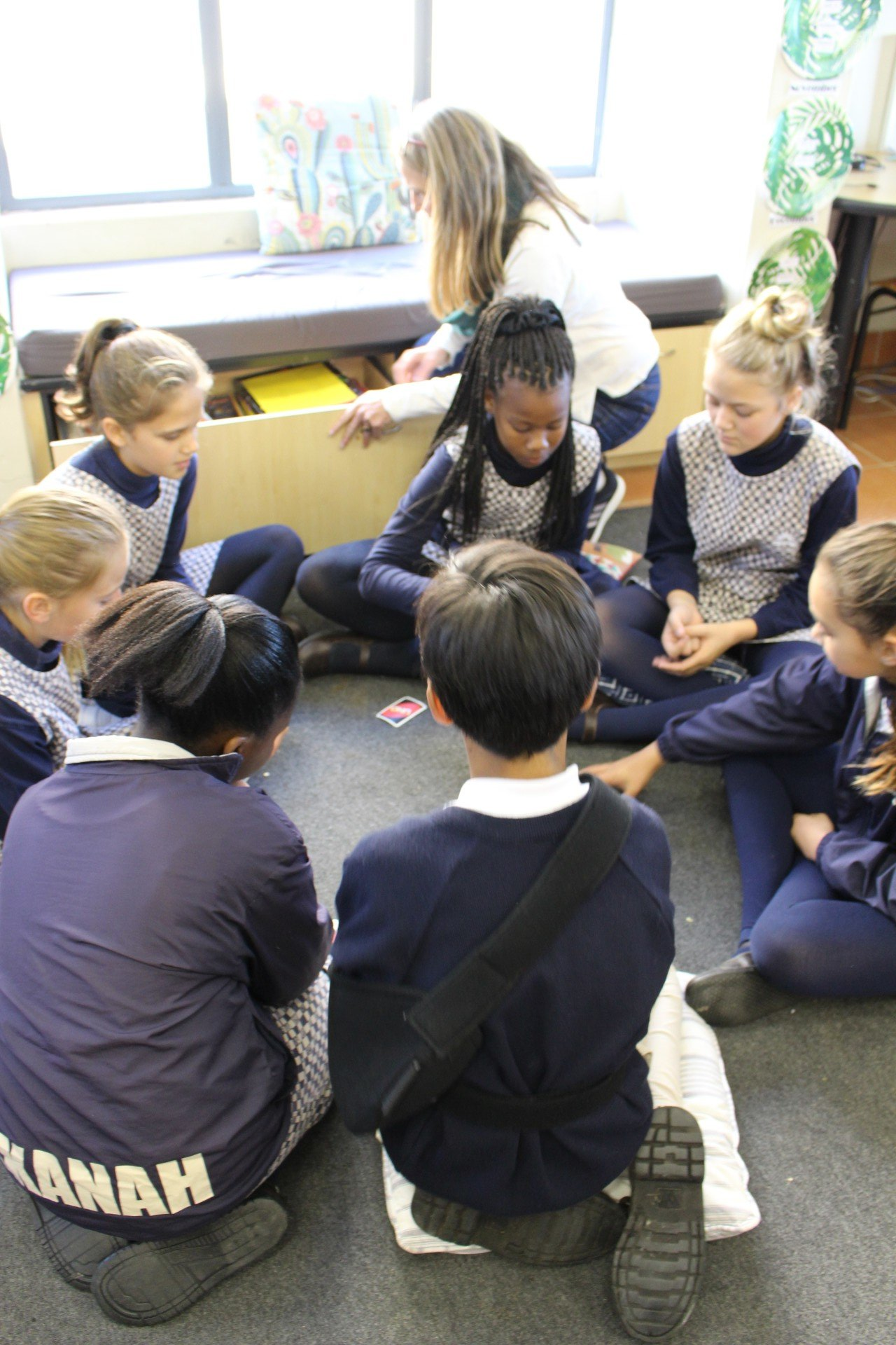 a group of children are sitting in a circle on the floor playing cards .