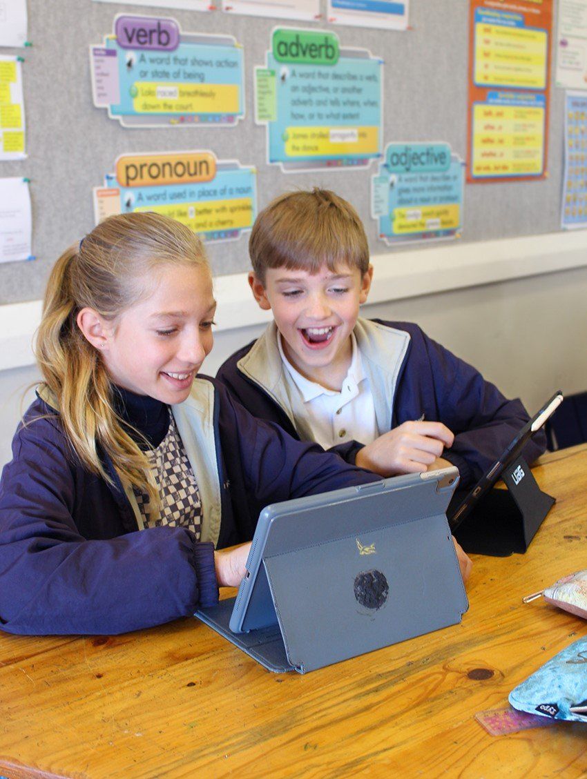 a boy and a girl are sitting at a table looking at a tablet .
