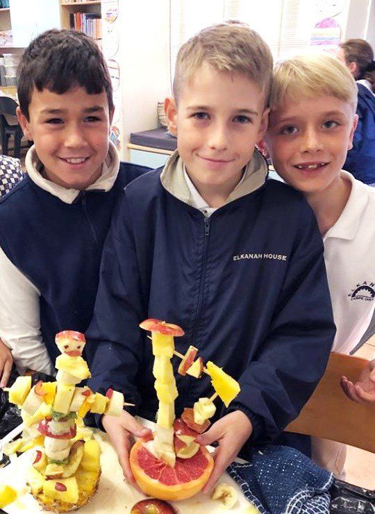 three young boys are posing for a picture with a fruit sculpture made out of fruit