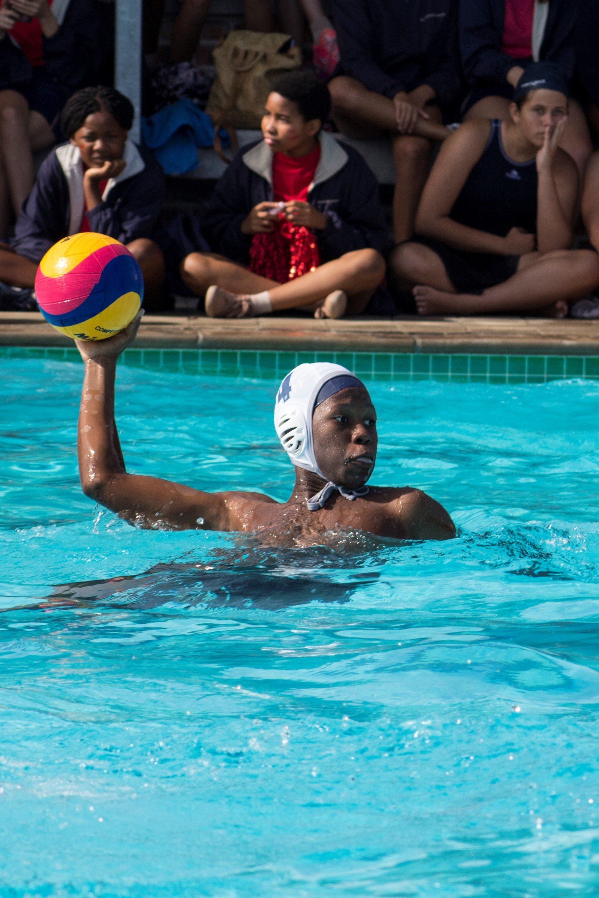 a boy is swimming in a pool holding a water polo ball