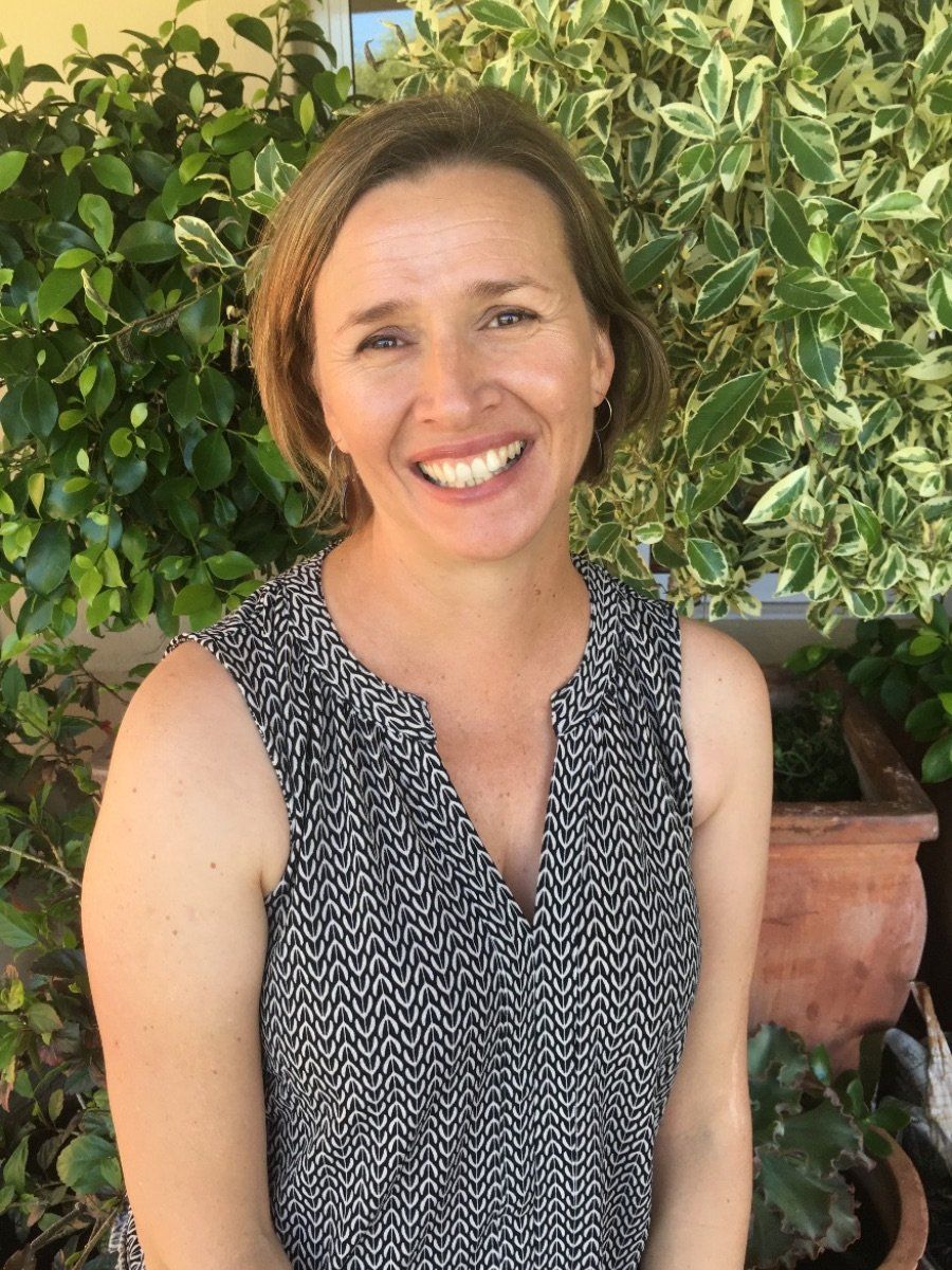 A woman in a black and white tank top is smiling in front of potted plants.