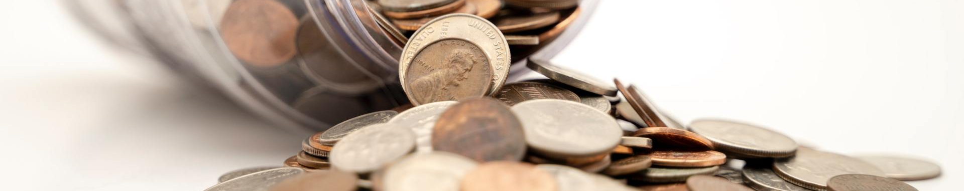 Coins are pouring out of a jar on a white surface.