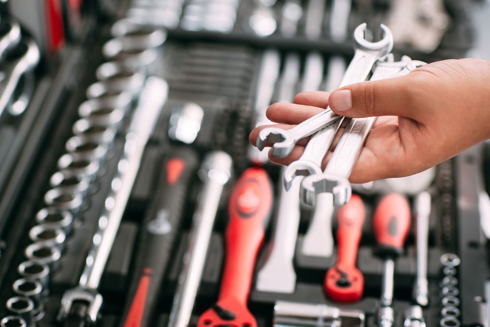 A person is holding a wrench in front of a toolbox filled with tools.