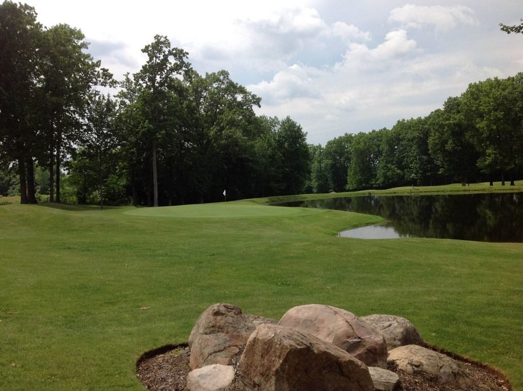 Green golf course with a pond and trees under a cloudy sky.