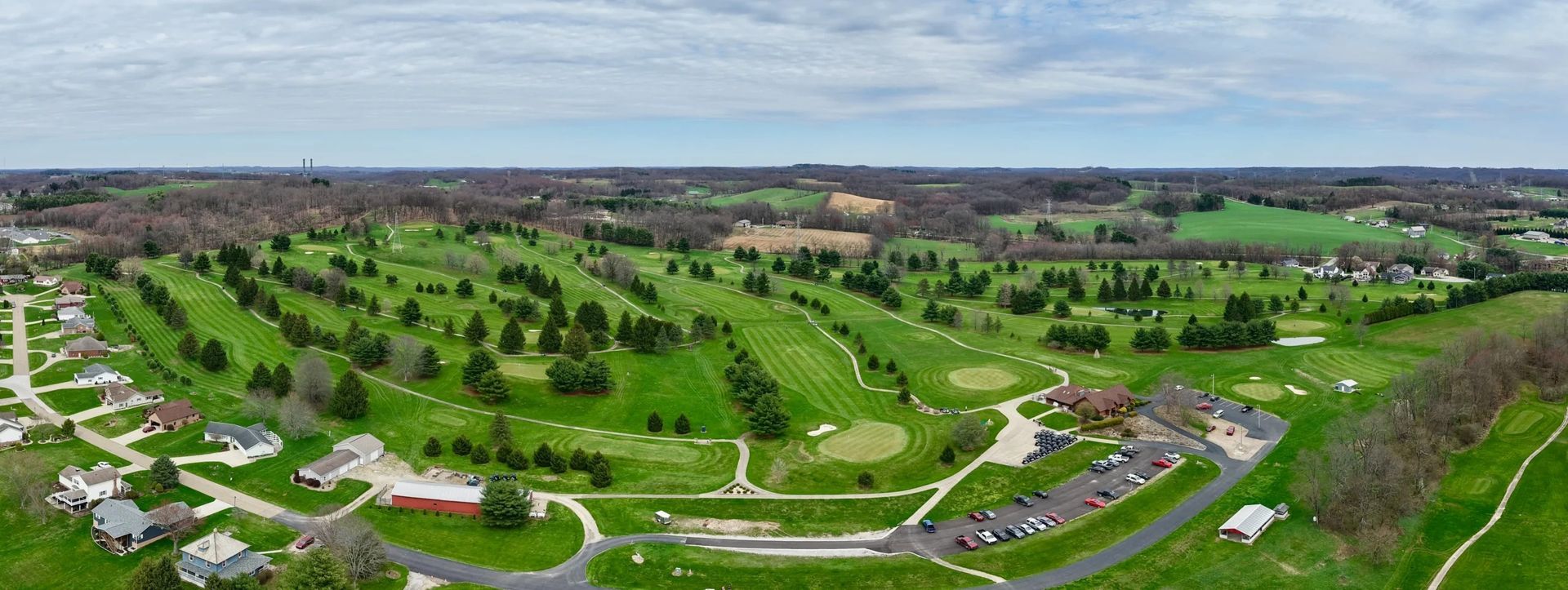 Aerial view of a golf course with green fairways, trees, and a clubhouse.