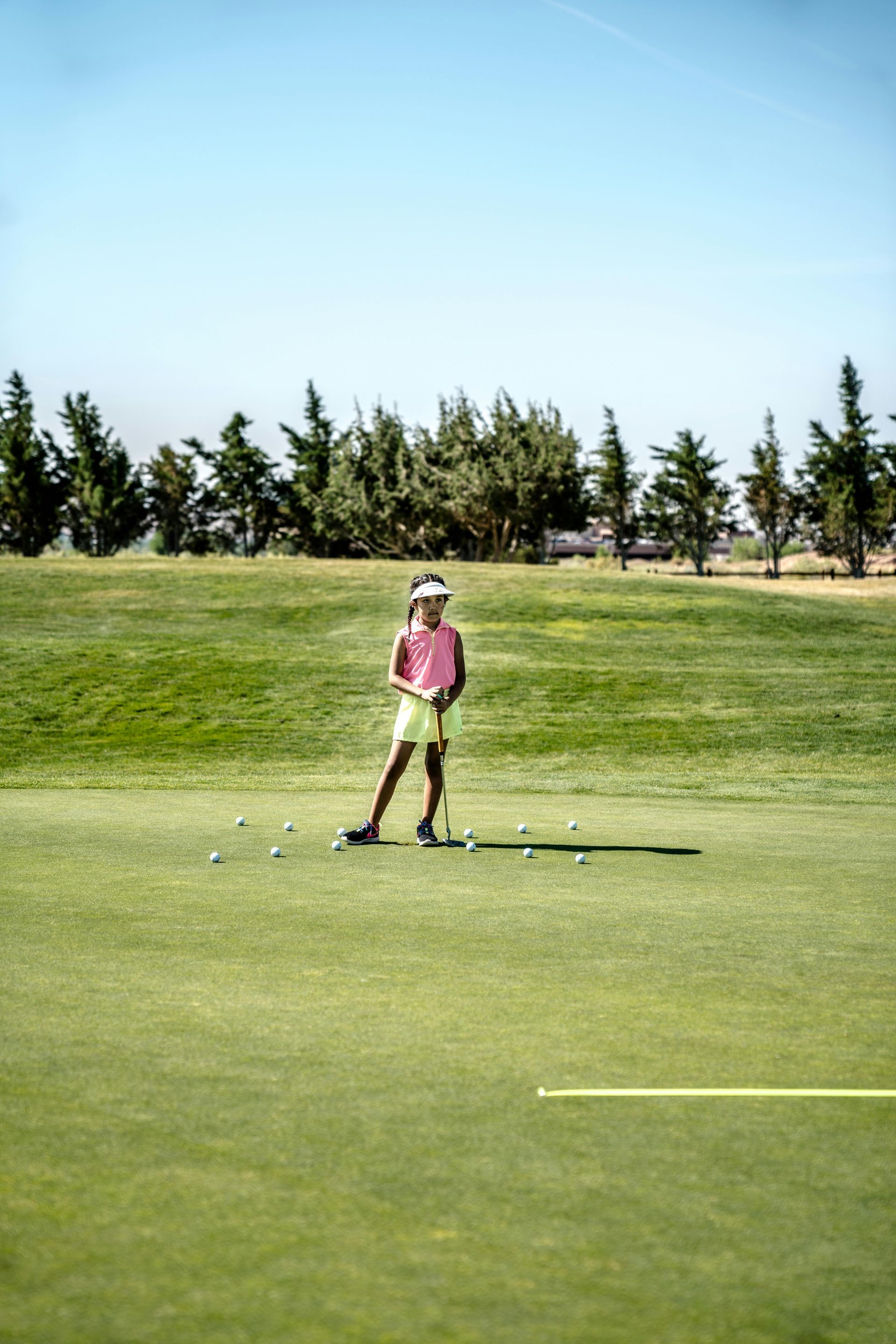 Young girl in pink golfing on a green field, under a blue sky.