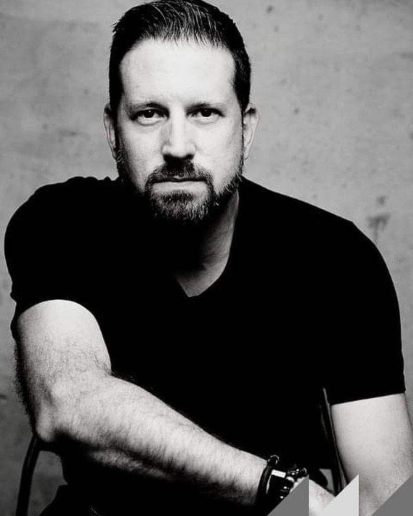 Man with a beard, black t-shirt, leaning forward; black and white photo.