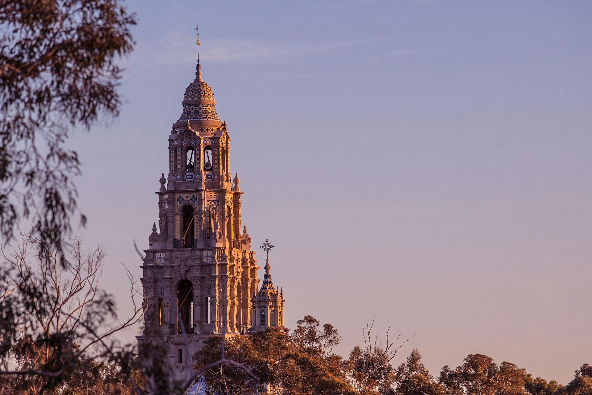 A large clock tower with a cross on top of it is surrounded by trees.