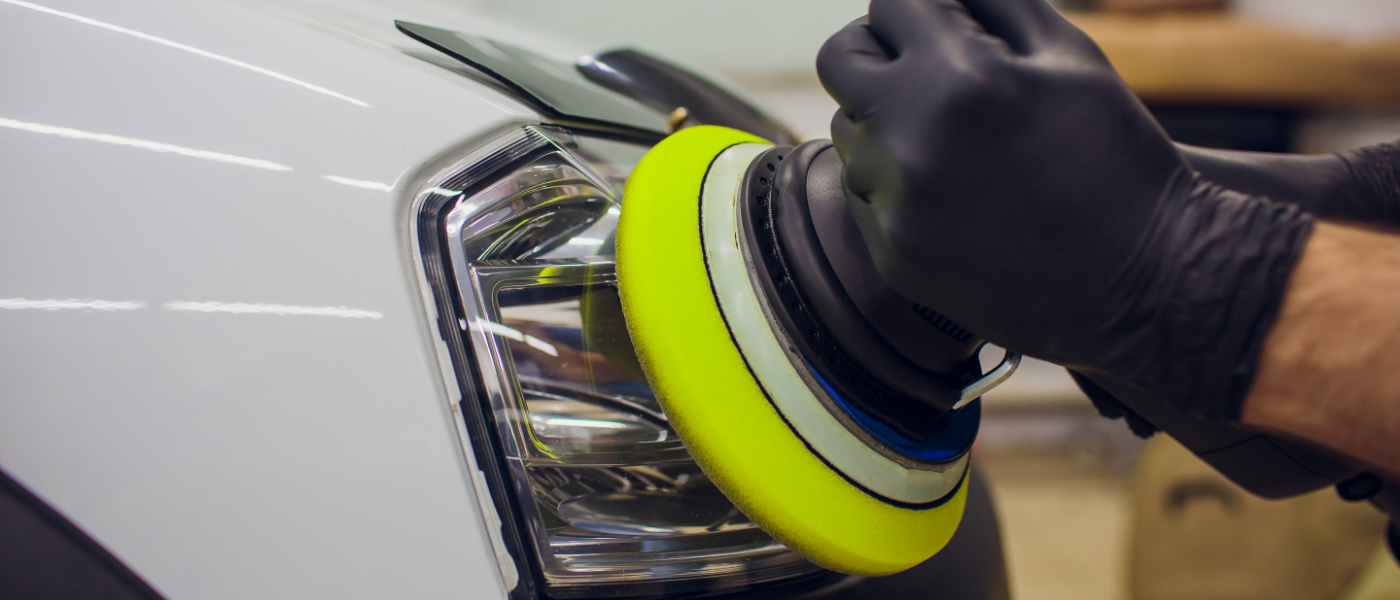 Photo of a mobile detailer professionally restoring and cleaning headlights on a sedan car. The headlights now look crystal clear