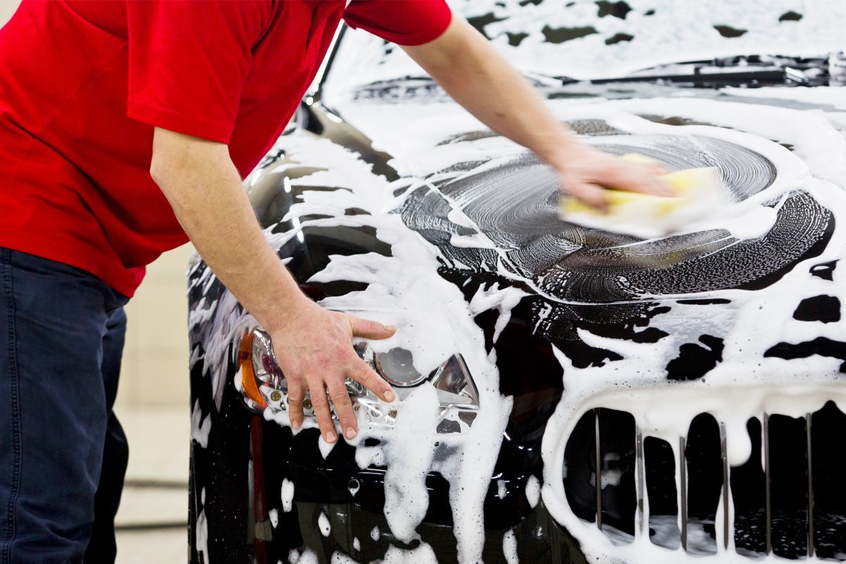 Person washing a black car with soapy suds and a sponge in Duluth, GA.