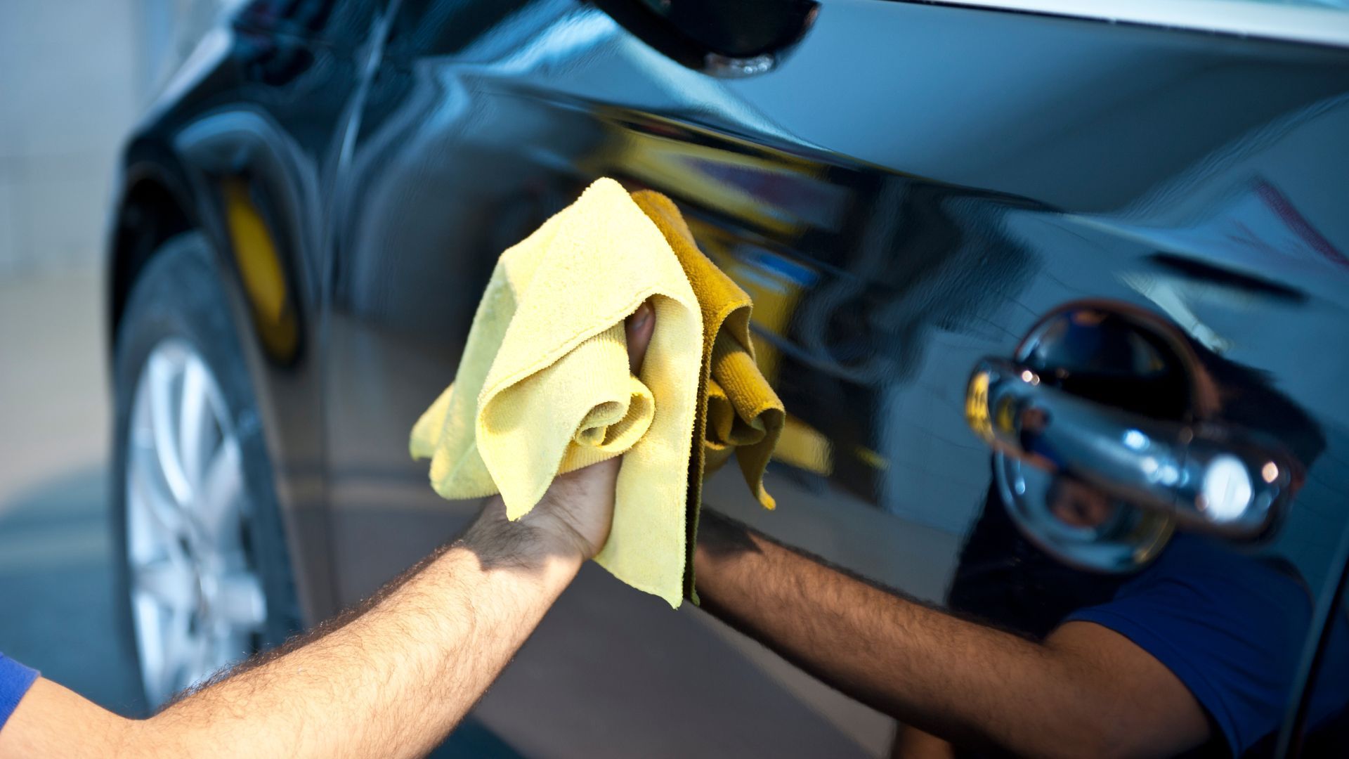 Hand polishing a shiny black car with a yellow cloth in Duluth, GA.