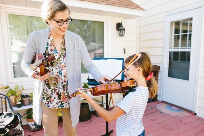 A woman is teaching a young girl how to play a violin.